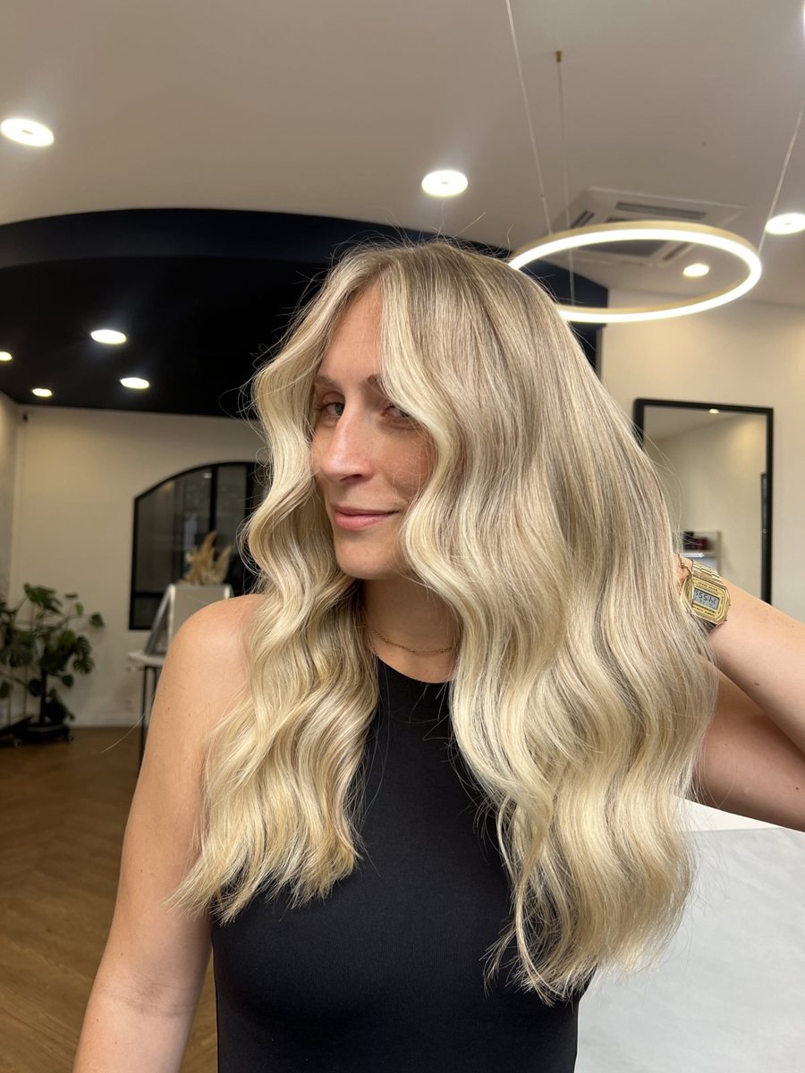 Balayage blond éclatant et ondulé réalisé en salon, idéal pour l'hiver